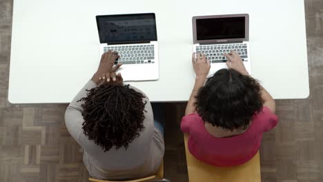 vista superior de las mujeres que trabajan con computadoras portátiles mientras están sentadas en la mesa