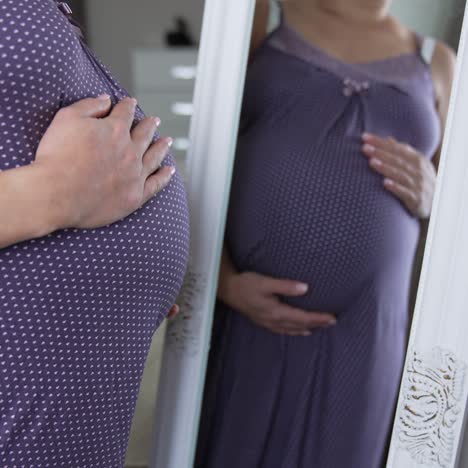 future mother with advanced pregnancy comes up to big mirror. woman in a long nightgown in front of the big mirror caressing the tummy with two hands. close up