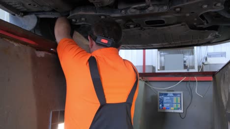 professional mechanic working under a car on a lift in an auto service shop