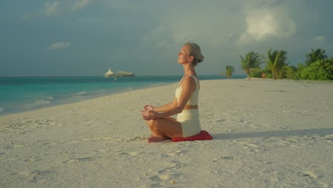 Woman-practicing-yoga-easy-pose-while-on-tropical-beach,-meditative-state