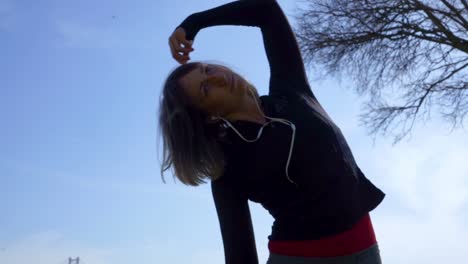 Low-angle-view-of-sporty-young-woman-exercising-against-blue-sky