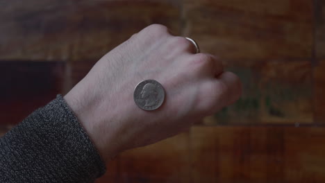el hombre revela la moneda en el dorso de su mano con piso de madera en el fondo
