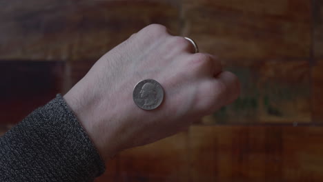 man reveals the coin at the back of his hand with wooden floor on the background