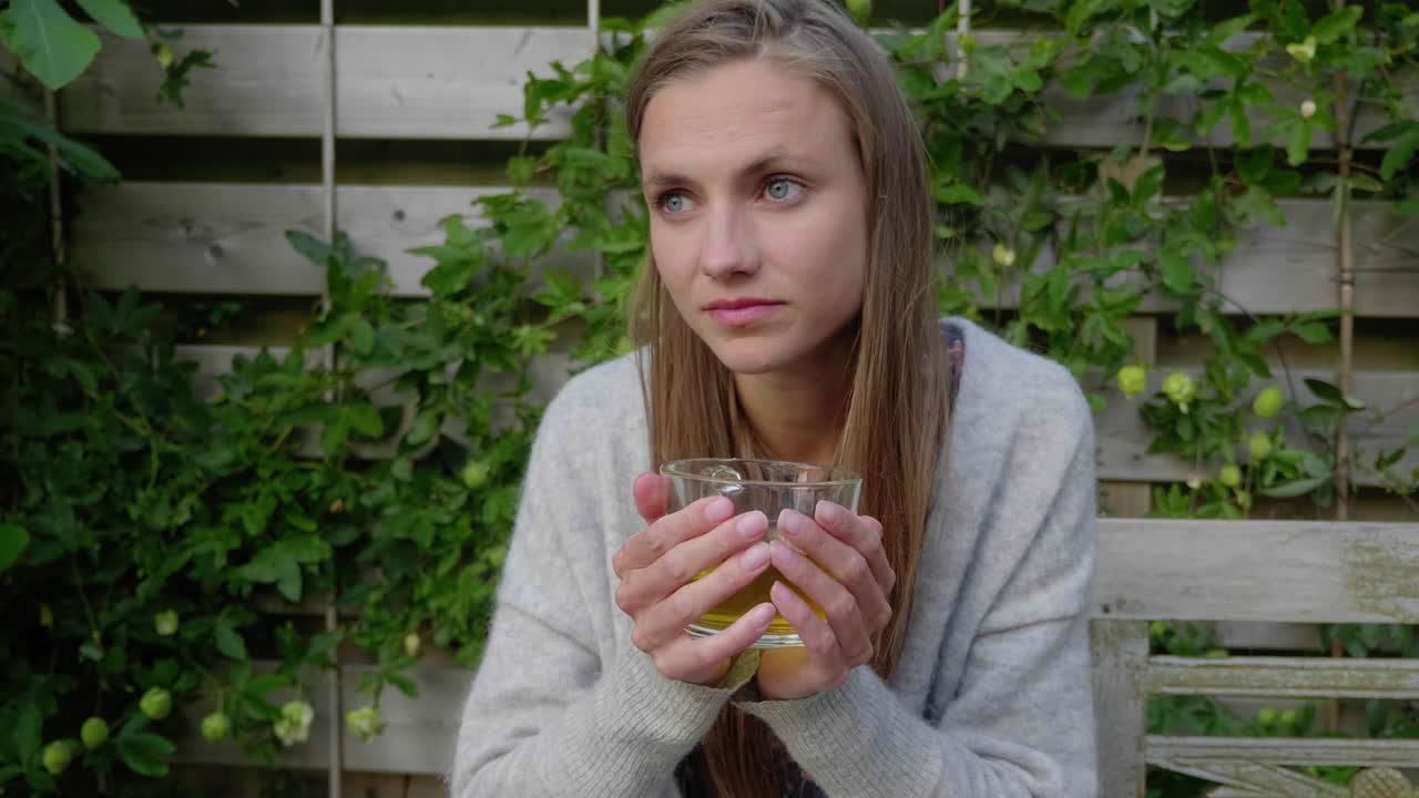 젊은 여자는 신중하게 정원에서 차 한잔을 즐기는 벤치에 앉아