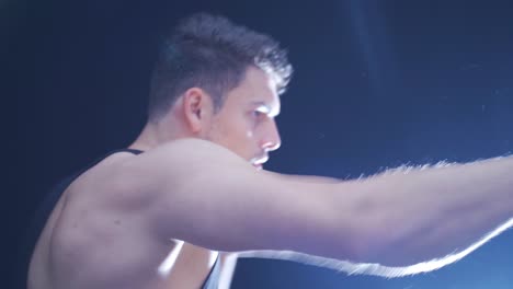 portrait of male boxer beating punching bag in dark gym.