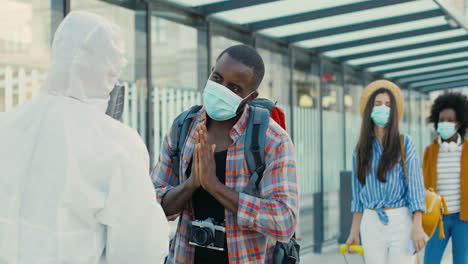 rear view of epidemiologists in white personal protective equipment measuring temperature in males and females people at bus station