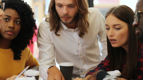 Close-up-view-of-multiethnic-coworkers-viewing-graphics-and-talking-sitting-at-a-table-in-a-cafe