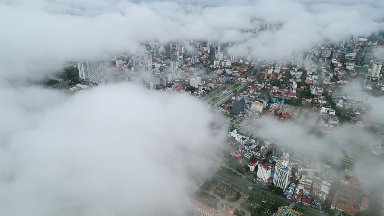 Aerial video of Phnom Penh city shrouded in misty clouds, with buildings and green boulevards peeking through