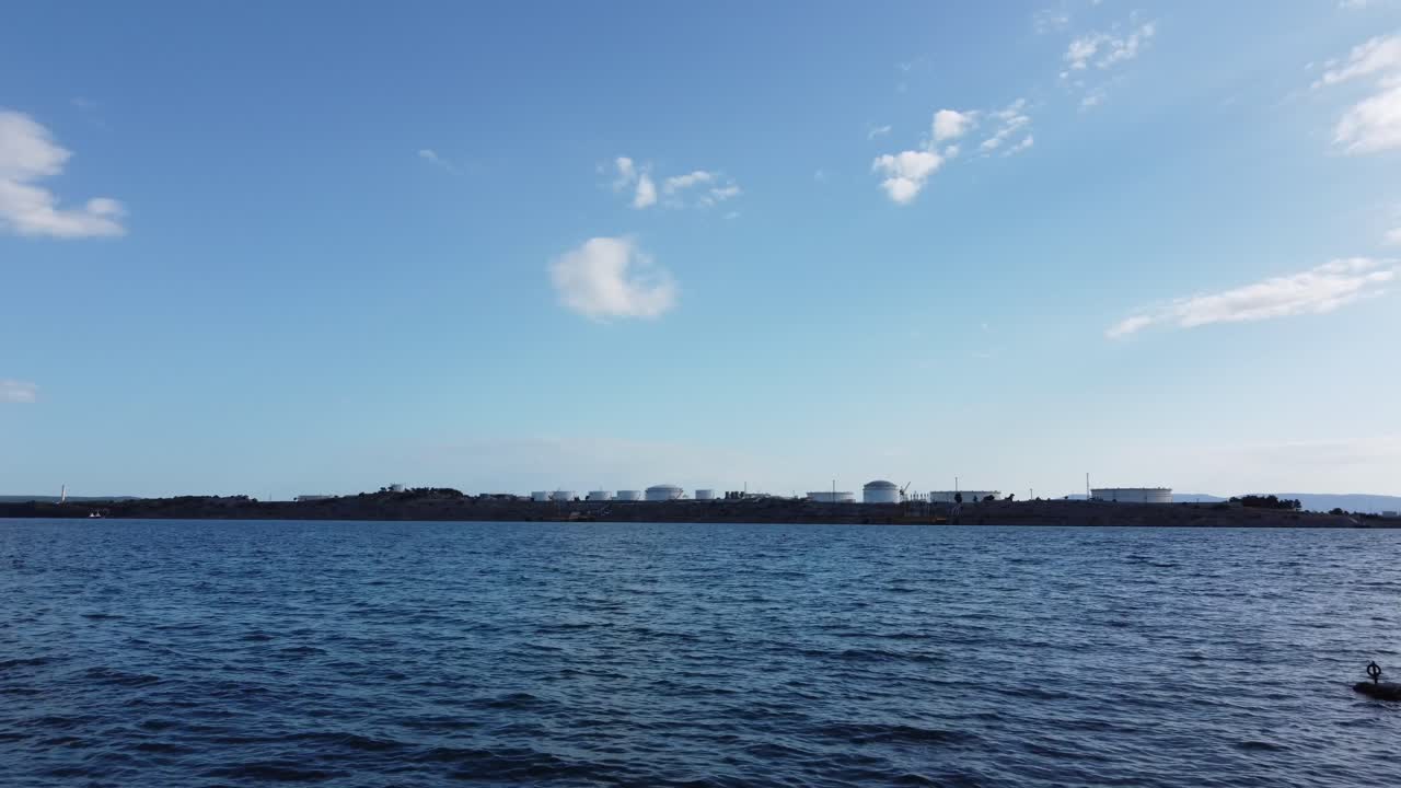 탱크와 파이프라인이 있는 크로에이션 섬에서 멀리 떨어진 물 위를 밀접하게 비행하는 드로나