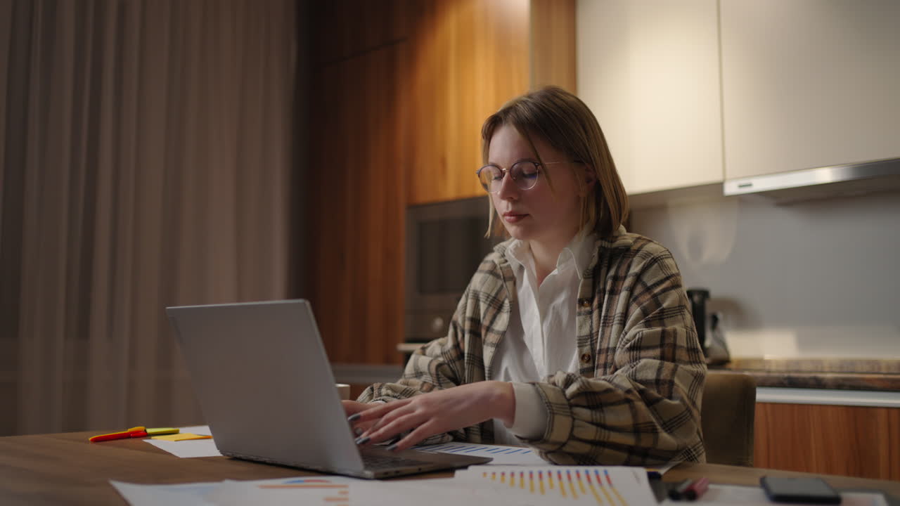 mujer de negocios madura que trabaja desde casa centrada mujer está trabajando con su computadora portátil y documentos en papel sentada en la cocina en casa. aplicación de computadora portátil calcular costos gastos presupuesto estimado para el proyecto