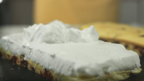 Close-up-of-whipped-egg-white-cream-being-put-on-a-delicious-swiss-roll-dough-by-a-vegan-chef-with-another-cake-in-the-background