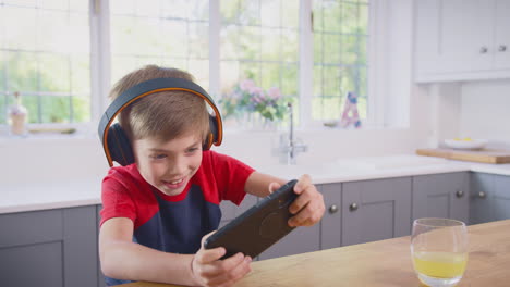 niño en casa en la cocina jugando al juego en el teléfono móvil usando auriculares inalámbricos