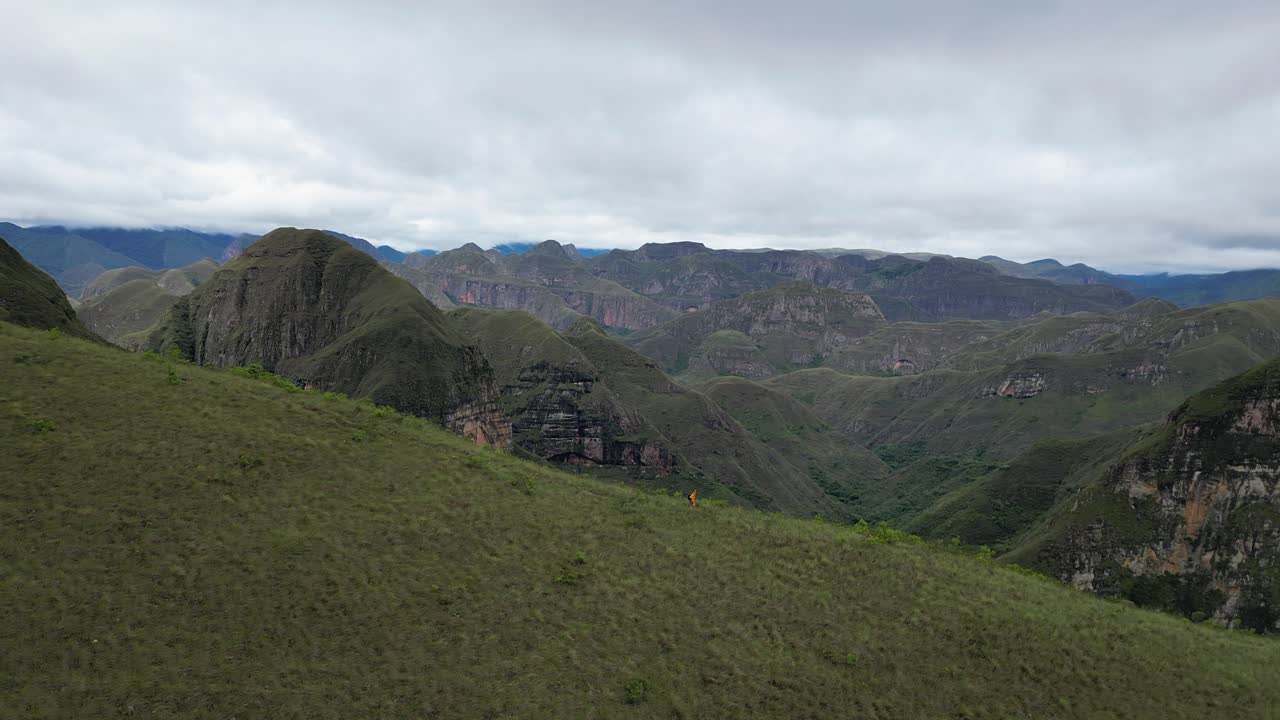 Aerial pulls back as hiker jogs down mountain ridge, Codo de los Andes