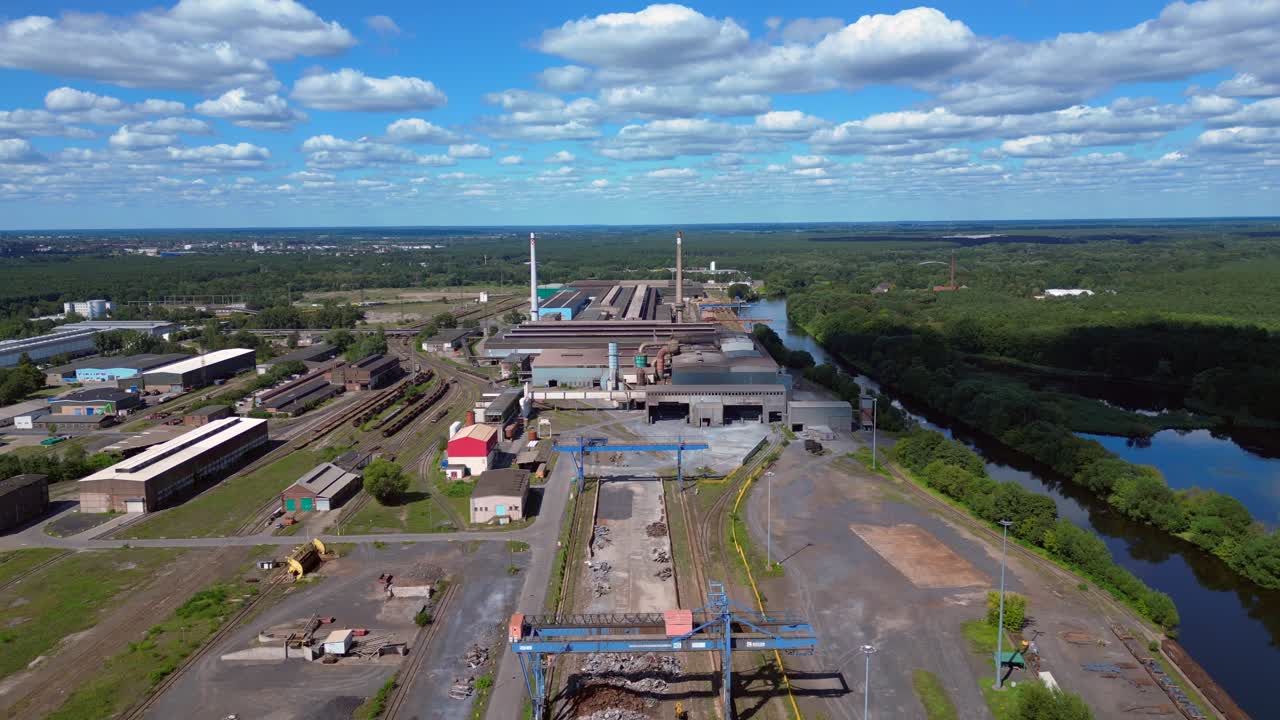 Hennigsdorf electric steel factory with train tracks, chimneys, and industrial buildings under a blue sky. Nice aerial view flight ascending drone