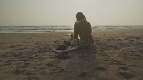 Silhouette-Einer-Frau,-Die-An-Einem-Strand-Zeichnet,-Von-Hinten-Aufgenommen,-Mit-Sanften-Wellen-Im-Hintergrund-–-Eine-Wunderschöne-Szene