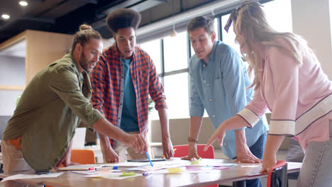 happy diverse colleagues brainstorming with documents and tablet at table in office in slow motion