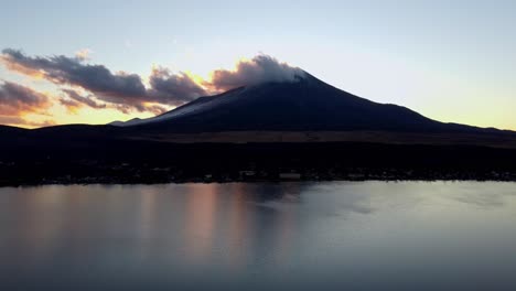 Mount-Fuji-silhouette-at-dusk,-reflecting-on-a-calm-lake-with-clouds