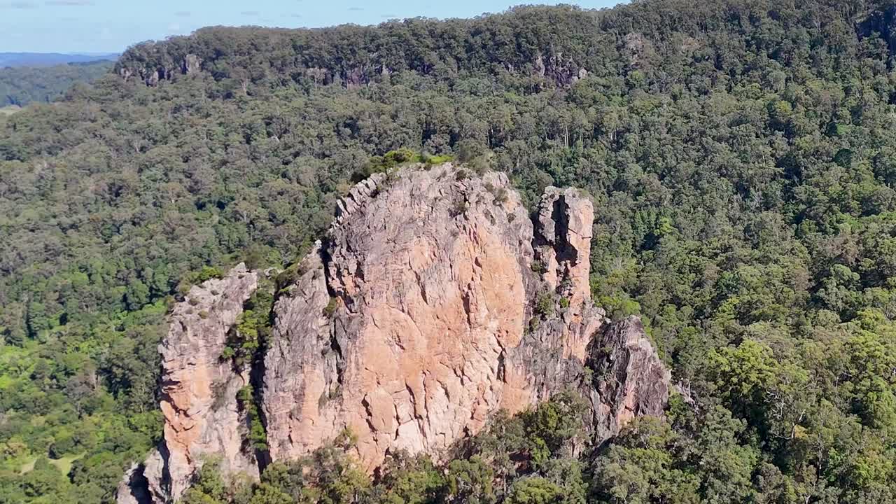 Drone footage captures towering volcanic rock formations surrounded by dense green forest under clear skies