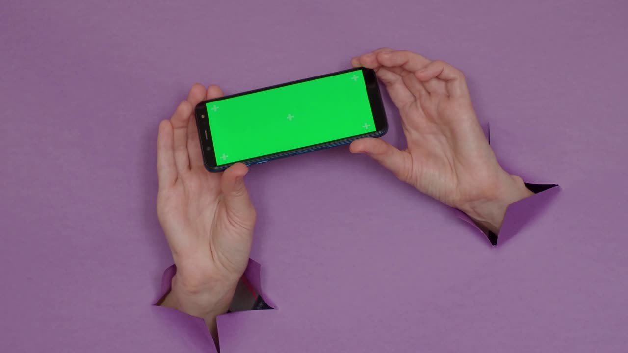 teléfono con una pantalla verde en las manos, sobre un fondo púrpura