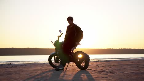 Footage-of-a-male-biker-leaning-on-his-bike-alone-in-front-the-water-in-sunlight