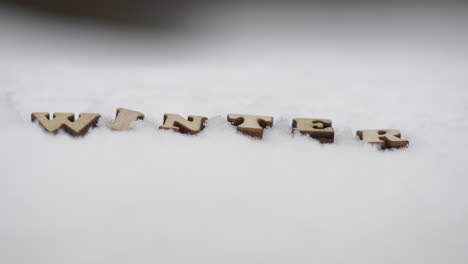 winter concept, intro title written with wooden letters in snow, winter landscape tilt up rack focus