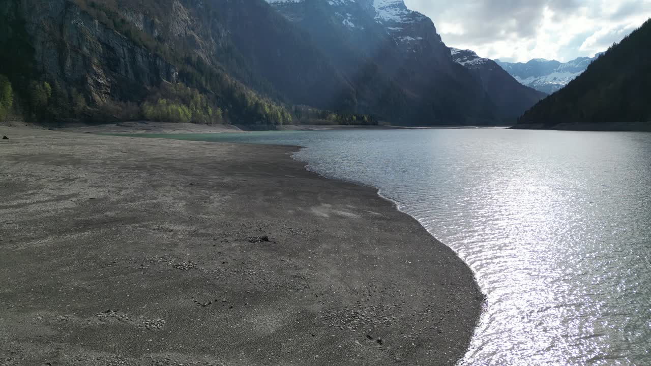 Aerial forward view of shoreline of an alpine lake in a fantastic mountain landscape