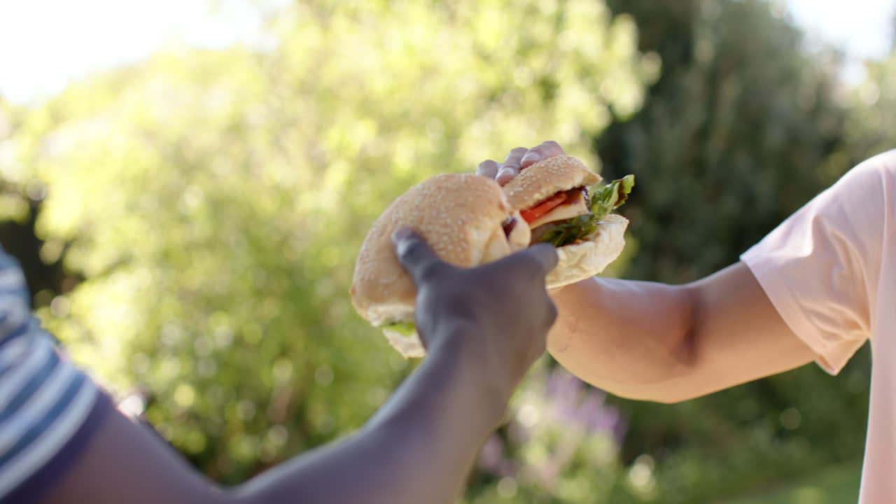 Holding burgers, two friends toasting together outdoors, enjoying time together, copy space