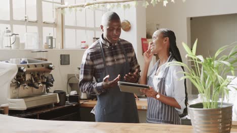 smiling african american female and male coffee shop owners talking and using tablet, slow motion