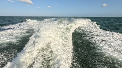 rastro de agua visto desde detrás de un barco a motor en rápido movimiento en un día de cielo despejado, mar azul, superficie del agua