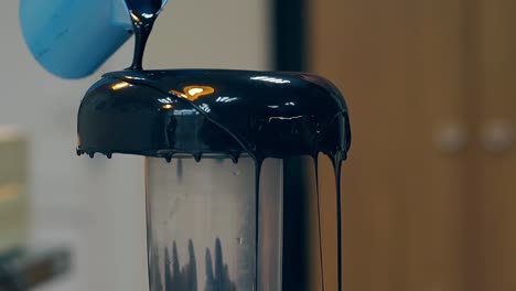 confectioner pours thick layer of dark chocolate on doughnut