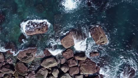 Overhead-aerial-descends-to-clear-green-sea-waves-on-rocky-coast-shore