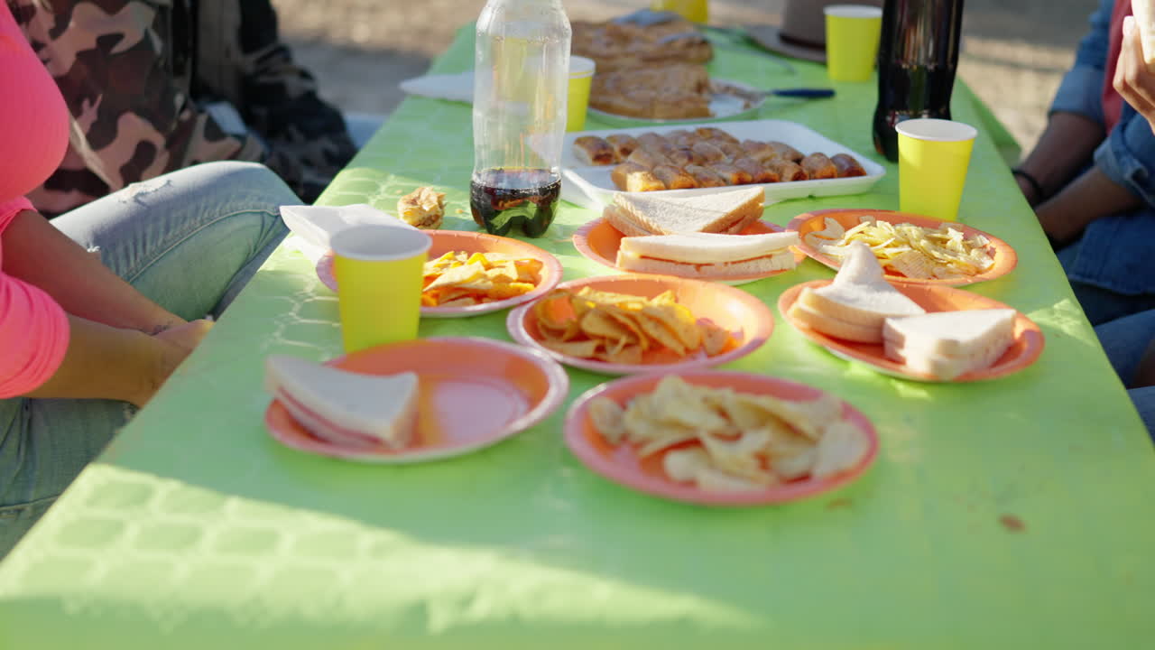 Outdoor picnic scene with a table full of snacks, sandwiches, and drinks