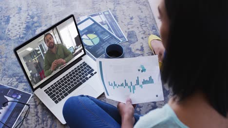 African-american-woman-holding-a-document-having-a-video-call-with-male-colleague-on-laptop