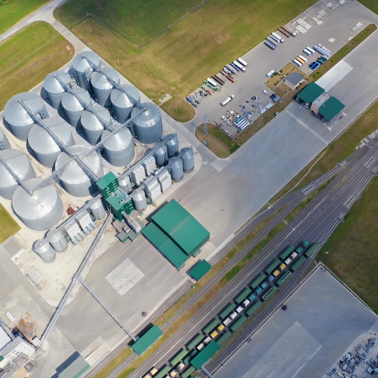 Grain silos. Aluminum containers for storage harvest. Railway with freight trains on industrial territory. Silver grain terminals on field. Top view. Agribusiness concept