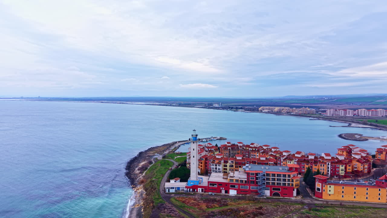 Vista della costa con faro ed edifici vicino alla riva durante il giorno in una città di mare