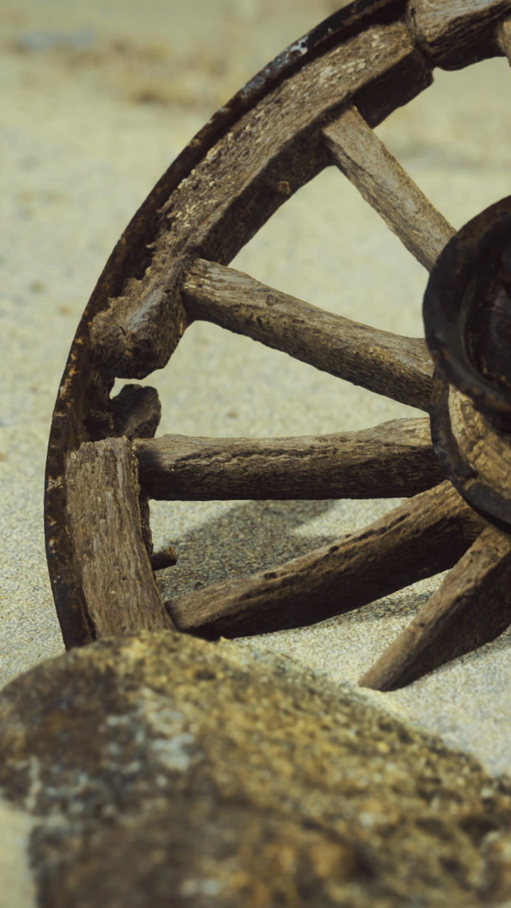 Old wooden wheel resting on sand near a rock at the beach