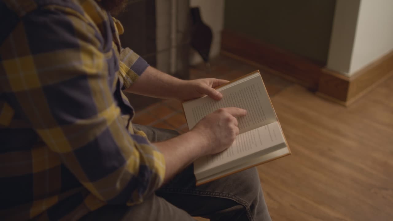 A man sitting, finding a page, reading, crossing his leg, and resting. Shot in 60 frames for slow motion
