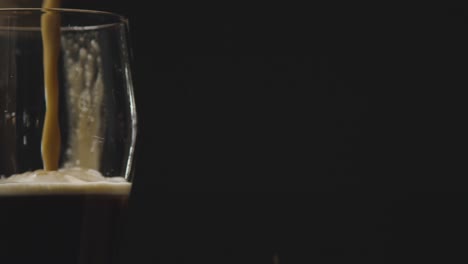 pint of irish stout being poured into glass against black studio background to celebrate st patricks day 3