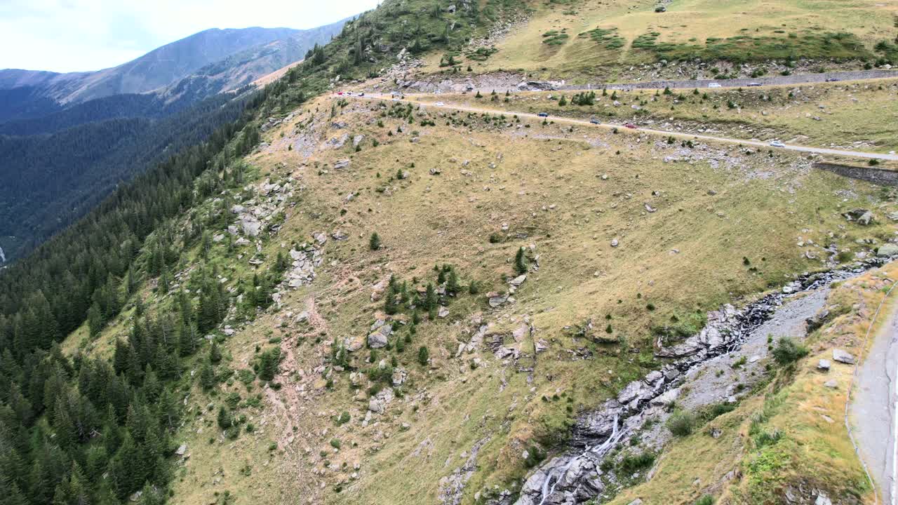 Un drone si innalza lentamente verso la cascata di Balea, la pineta e una strada di montagna tortuosa
