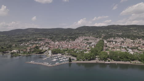 drone disparado volando sobre el lago bolsena en italia viniendo del agua a la antigua ciudad medieval con un castillo y edificios antiguos en la colina y un pequeño puerto en un día soleado