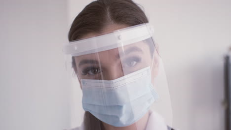 redhead doctor woman in white coat wearing medical mask and facial screen protection looking at the camera