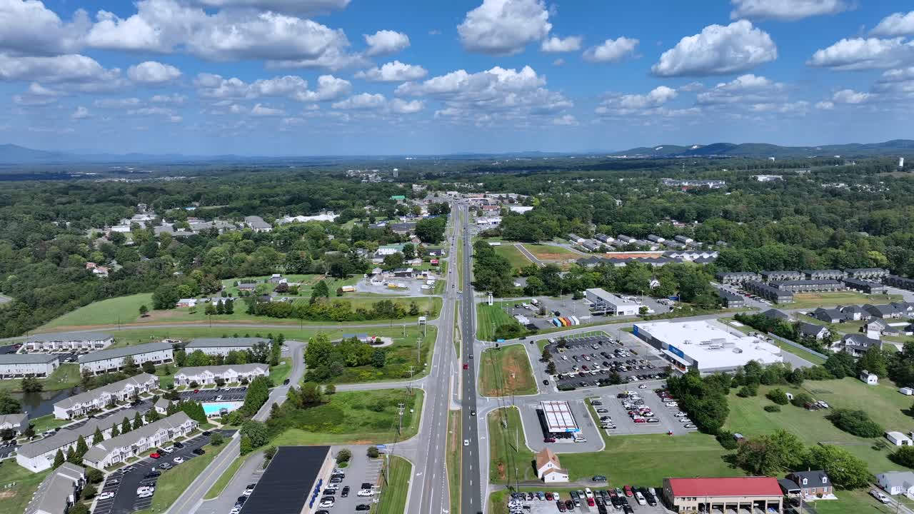 Ripresa aerea all'indietro del traffico su un'autostrada americana in periferia. Centro commerciale e nuova area residenziale sviluppata con piscina. Ampia inquadratura panoramica in estate.