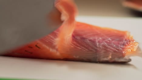 extreme close-up caucasian hand slices a thin layer of smoked salmon with knife