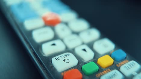 A-macro-close-up-shot-of-a-black-TV-remote-with-white-and-colorful-buttons,-studio-lighting,-slow-motion,-120-fps,-Full-HD