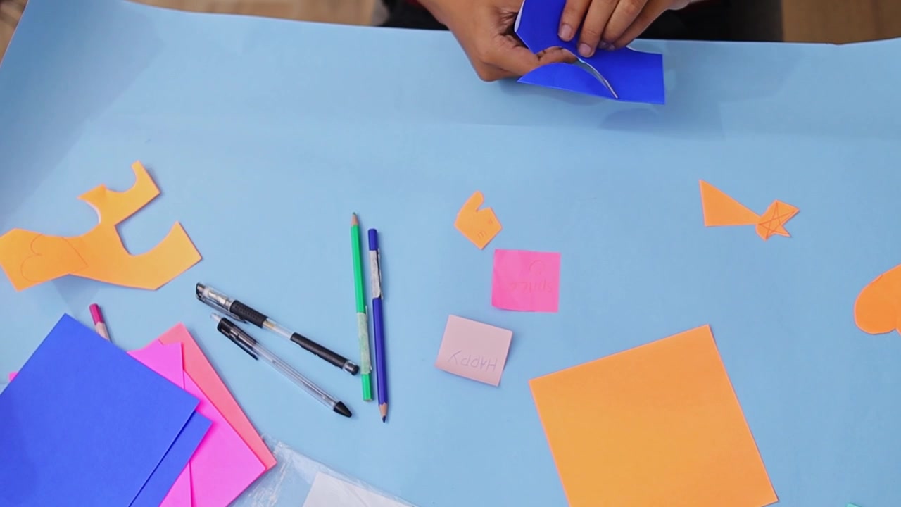 Primo piano di mani impegnate in un progetto creativo fai-da-te, che tagliano e piegano carta colorata su un piano di lavoro.