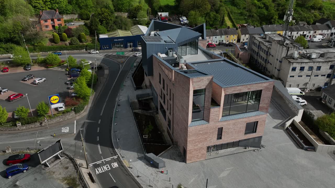 Peace Campus, County Monaghan, Ireland, April 2024. Drone orbits counter clockwise around Monaghan County Museum above Plantation Road with light vehicle traffic under a dark cloudy sky.
