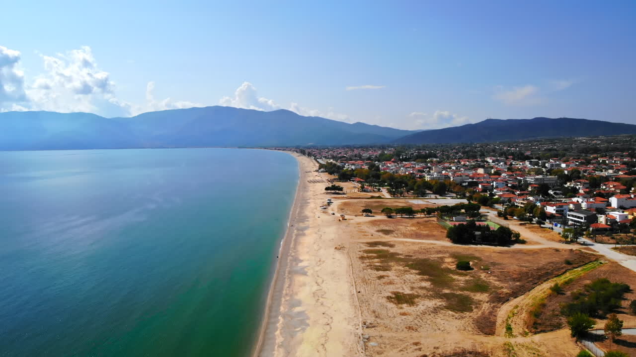 Panorama of the Asprovalta with multiple buildings and greenery, green hills on the background. Aegean sea coast. Long beach along the town. Sunny day. Greece