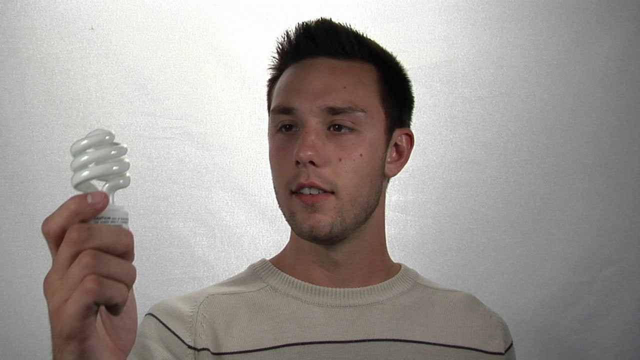 un hombre sostiene una bombilla fluorescente compacta en una mano y dinero en la otra