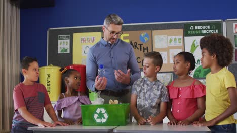 Diverse-teacher-and-schoolchildren-standing-in-classroom-learning-about-recycling-trash