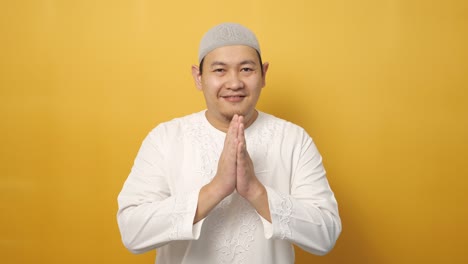 hombre musulmán asiático sonriendo y mostrando un gesto de saludo contra un fondo amarillo, concepto de celebración islámica del ramadán o eid fitr